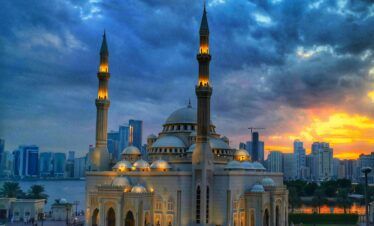 Gran Mezquita de Sharjah al atardecer con el skyline de la ciudad al fondo durante el tour cultural desde Dubái con Passion Dubai Tours