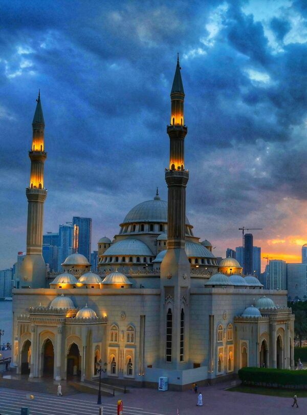 Gran Mezquita de Sharjah al atardecer con el skyline de la ciudad al fondo durante el tour cultural desde Dubái con Passion Dubai Tours