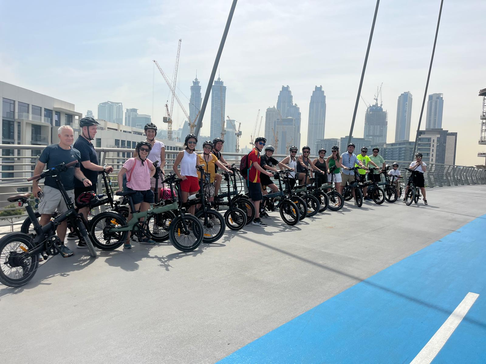 Grupo de turistas en el tour en bicicleta eléctrica por Dubái con el skyline de fondo