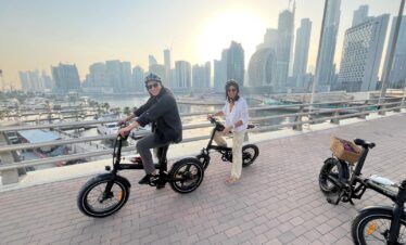 Turistas en el tour en bicicleta eléctrica por la Marina de Dubái con el skyline de fondo